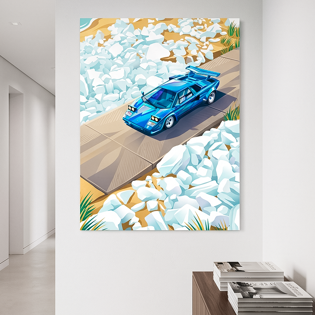A vertical canvas wall art print depicting a blue sports car on a road surrounded by white rocks, displayed on a white wall in a modern hallway above a wooden console table with magazines.